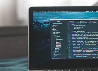 A laptop displaying a code editor with lines of code related to a React application. The screen shows project folders and files written in JavaScript, suggesting software development in progress. The background is slightly blurred, adding focus to the laptop screen.