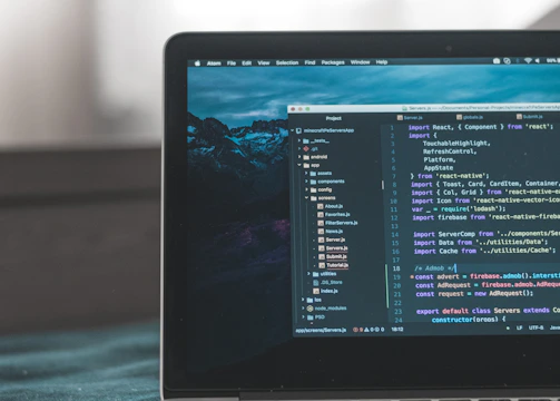 A laptop displaying a code editor with lines of code related to a React application. The screen shows project folders and files written in JavaScript, suggesting software development in progress. The background is slightly blurred, adding focus to the laptop screen.