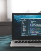 A laptop displaying a code editor with lines of code related to a React application. The screen shows project folders and files written in JavaScript, suggesting software development in progress. The background is slightly blurred, adding focus to the laptop screen.