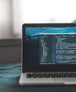A laptop displaying a code editor with lines of code related to a React application. The screen shows project folders and files written in JavaScript, suggesting software development in progress. The background is slightly blurred, adding focus to the laptop screen.