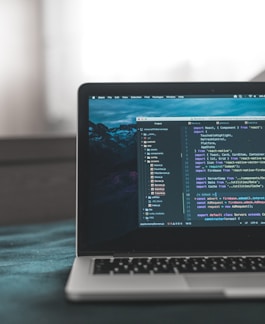 A laptop displaying a code editor with lines of code related to a React application. The screen shows project folders and files written in JavaScript, suggesting software development in progress. The background is slightly blurred, adding focus to the laptop screen.