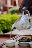 Artisan hands gently pouring golden ayurvedic oil into a small glass bowl, framed by fresh leaves.