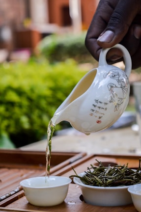 Artisan hands gently pouring golden ayurvedic oil into a small glass bowl, framed by fresh leaves.