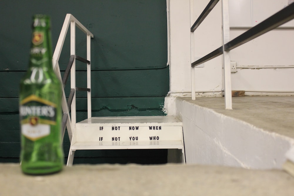 Botella de vidrio verde de pie cerca de una escalera de concreto gris