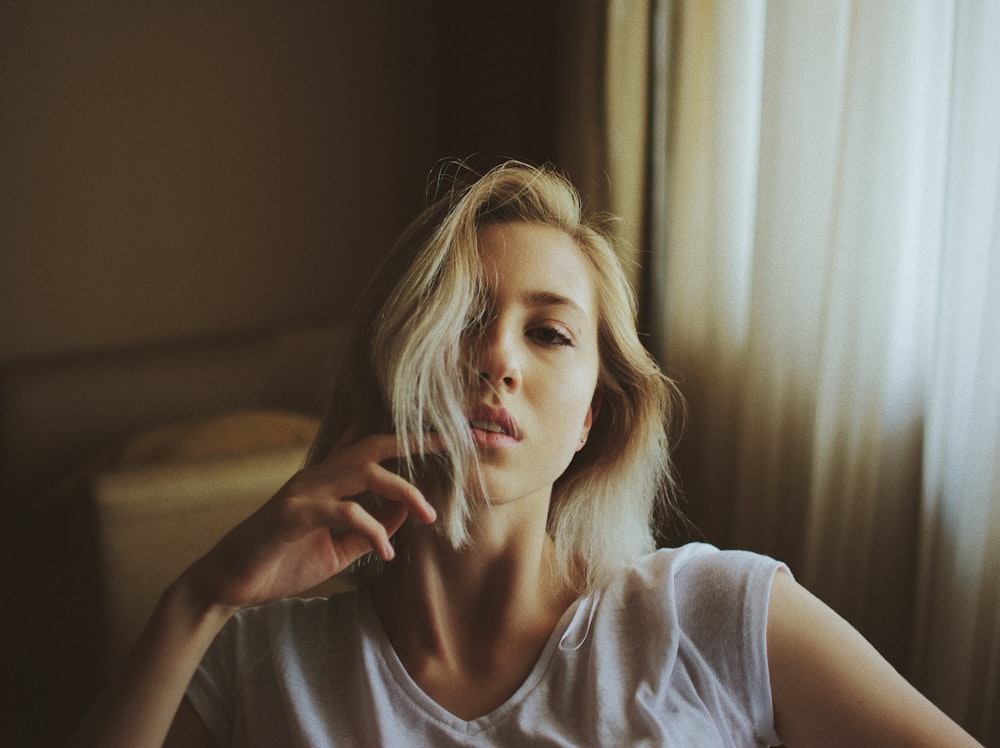 woman wearing white V-neck shirt standing beside white window curtain