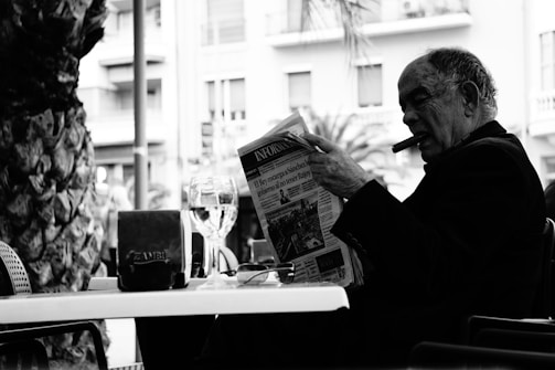 Middle-aged man enjoying a drink at a café table with a prostate cancer awareness coaster beneath his glass.