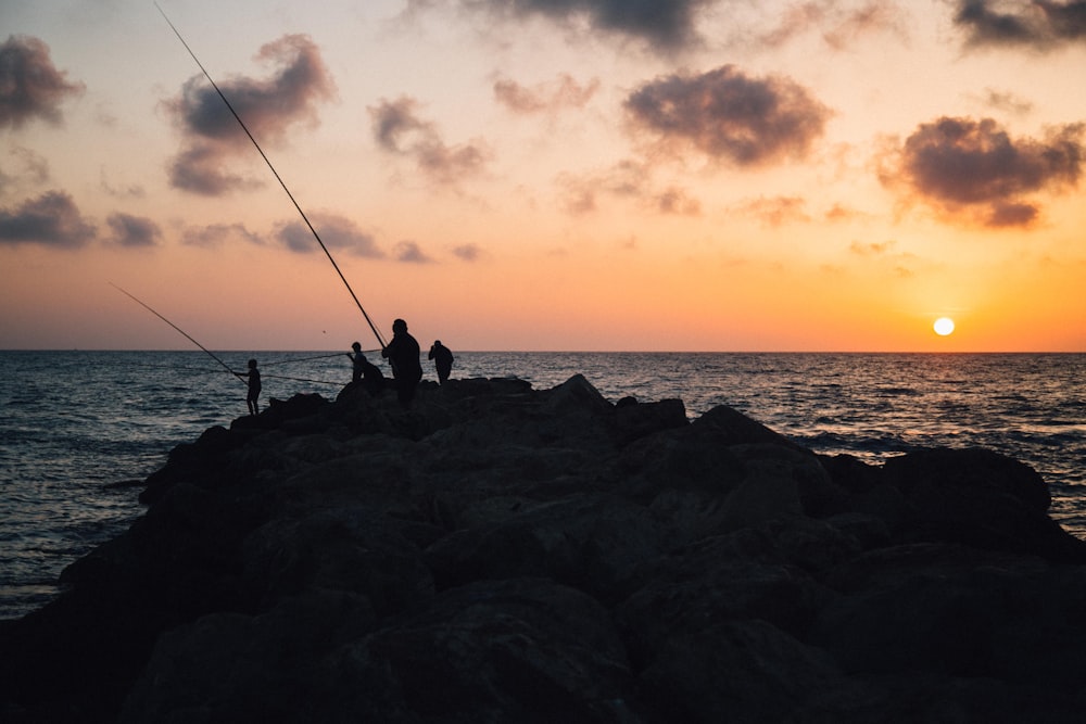 quatre personnes tenant des cannes à pêche face à la mer au coucher du soleil