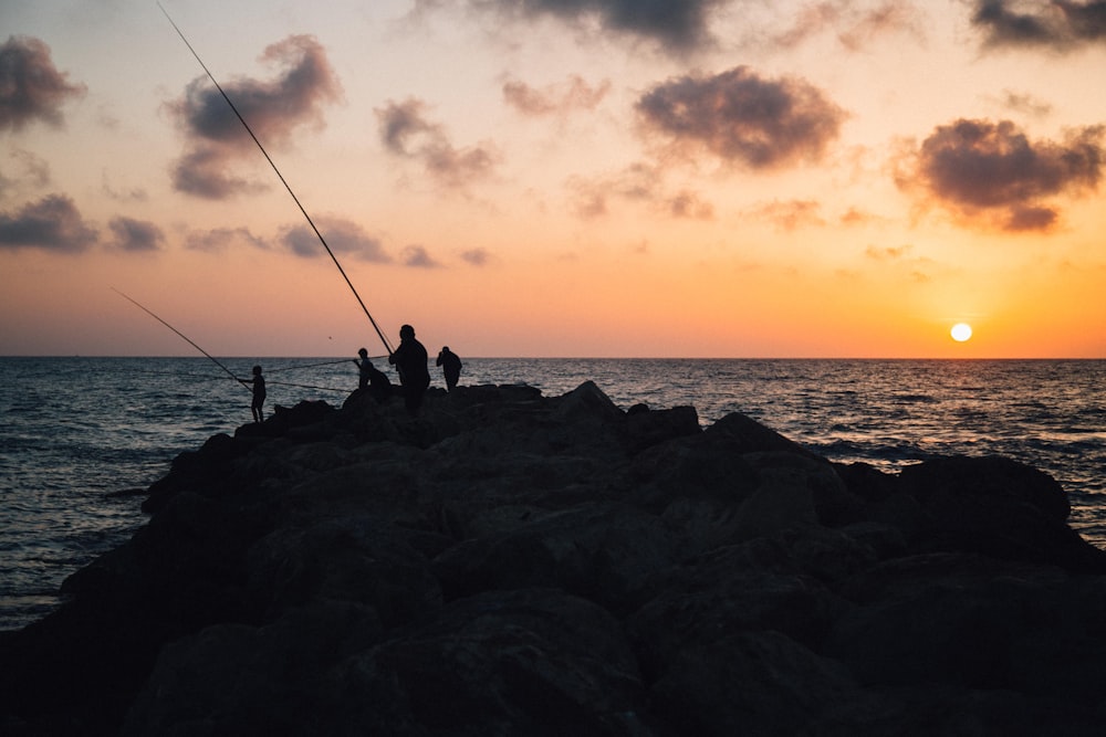 four people holding fishing rods facing sea at sunset