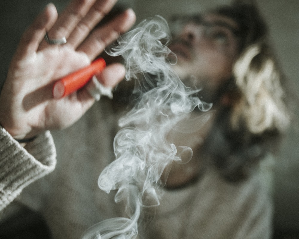 Fotografía de enfoque superficial de hombre sosteniendo encendedor desechable rojo