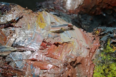 Thick, textured brushstrokes of oil paint in earthy tones and hints of yellow and blue create an abstract composition. The paint appears layered and mixed directly on the surface, resulting in a rich, tactile appearance.