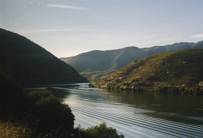 A serene landscape featuring a calm river flowing through gentle hills under a clear blue sky.