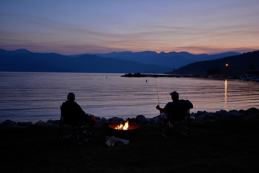 silhouette of two men next to calm body of water