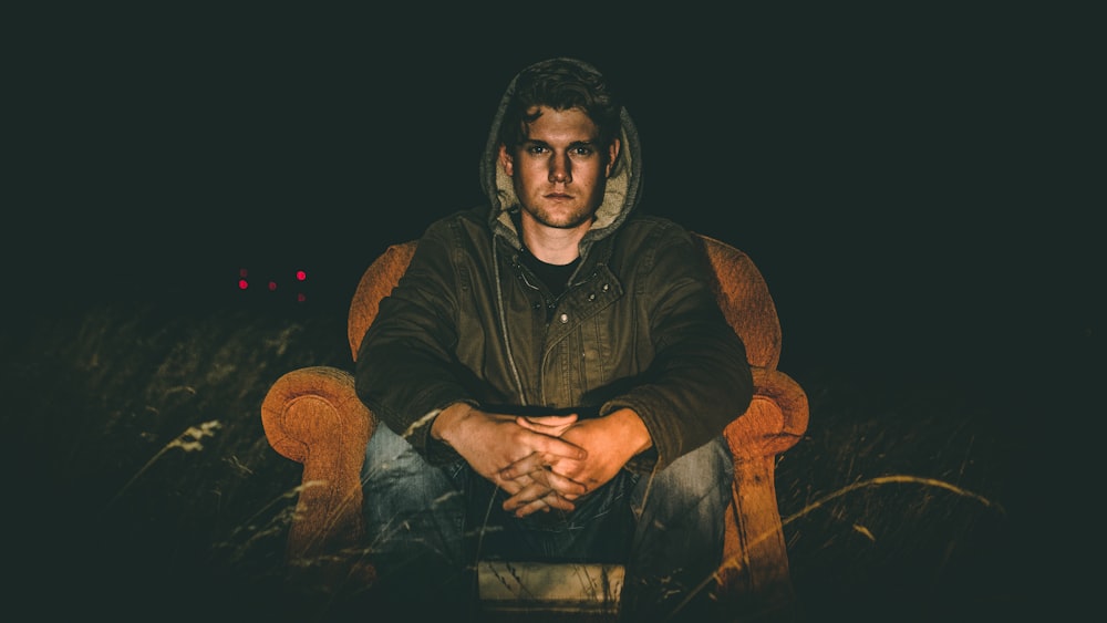 man wearing black zip-up hooded jacket sitting on sofa chair