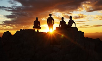 silhouette photography of four person on cliff during sunset