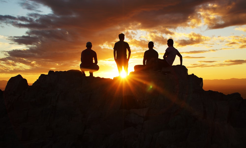 silhouette photography of four person on cliff during sunset