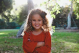 A joyful black teenage girl with natural curls smiling brightly in a sunlit park.