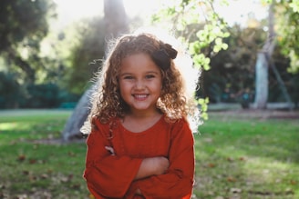 A vibrant outdoor portrait of a young girl with curly hair and a bright, joyful smile.