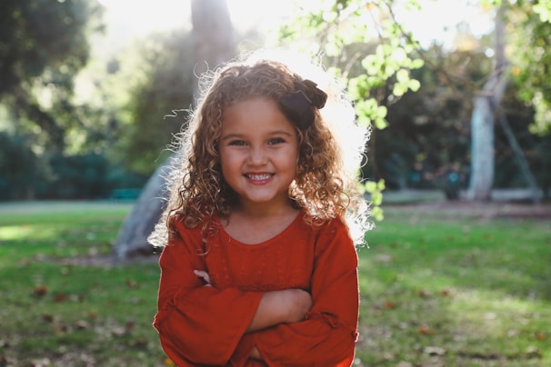 A vibrant outdoor portrait of a young girl with curly hair and a bright, joyful smile.