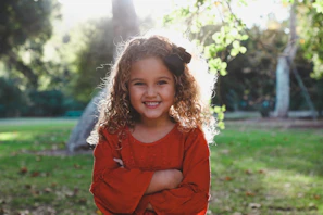 A joyful black teenage girl with natural curls smiling brightly in a sunlit park.
