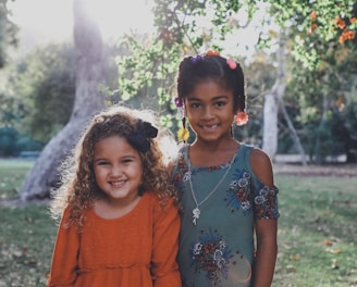 two dressed children standing against trees