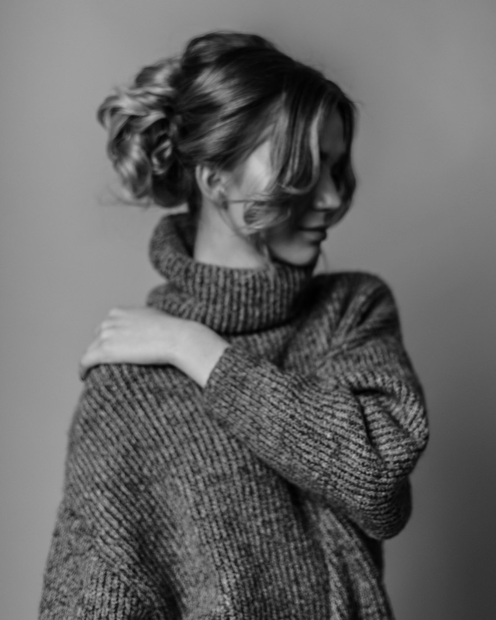 woman wearing turtleneck sweater touching her shoulder with her left hand grayscale photo