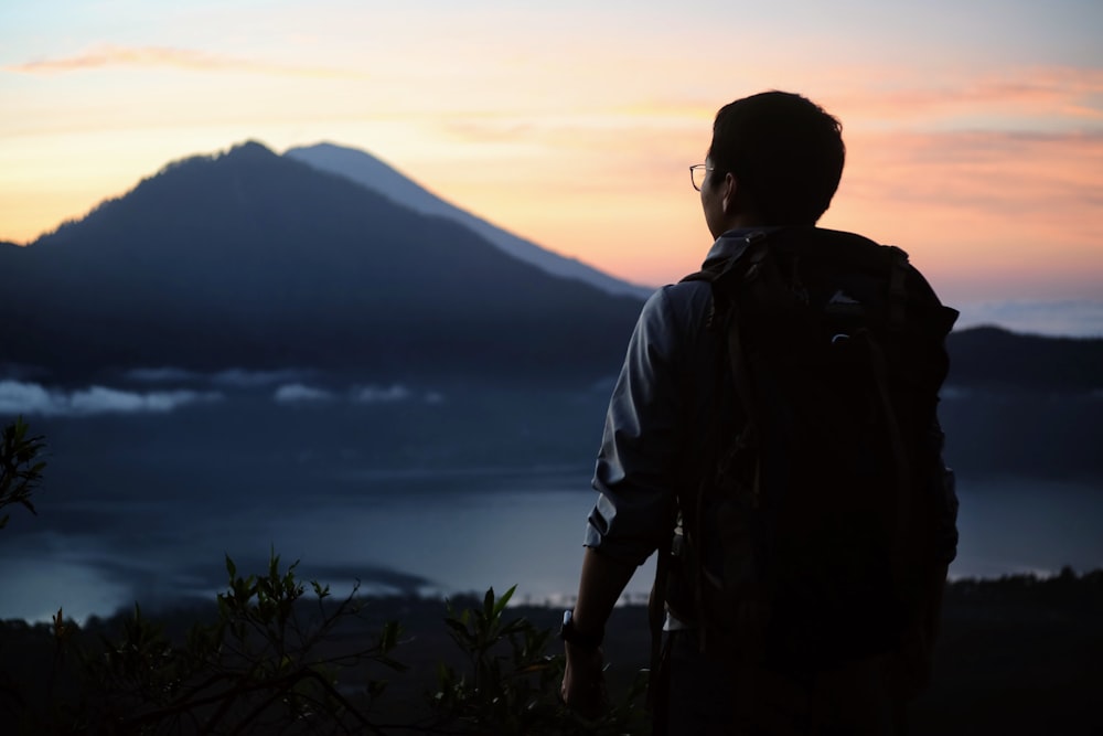 man wearing black backpack standing and watching mountain
