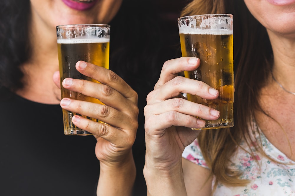 tow woman holding clear glass full drinking glasses