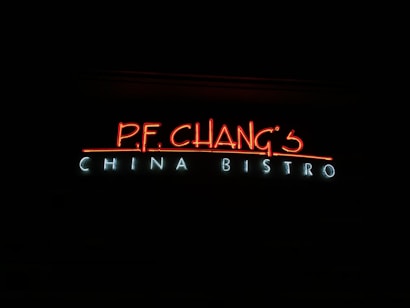 The image displays a glowing neon sign against a dark background. The sign reads 'P.F. Chang's China Bistro' with 'P.F. Chang's' in bright red and 'China Bistro' in a cooler light blue.