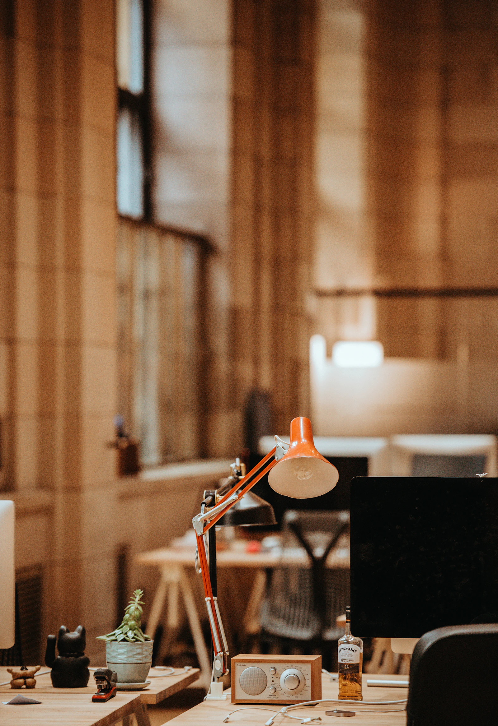 Warm workspace with desk lamp illuminating a monitor displaying code, the reading side of the engineering loop.