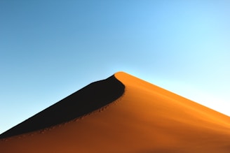Close-up of sand dunes with a sandboard resting on the golden sand, footprints leading away.