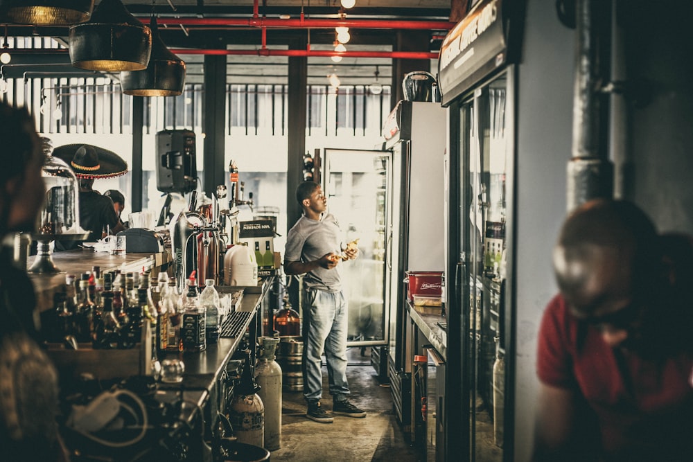 personne en haut gris debout devant le réfrigérateur près de la table avec des bouteilles d’alcool