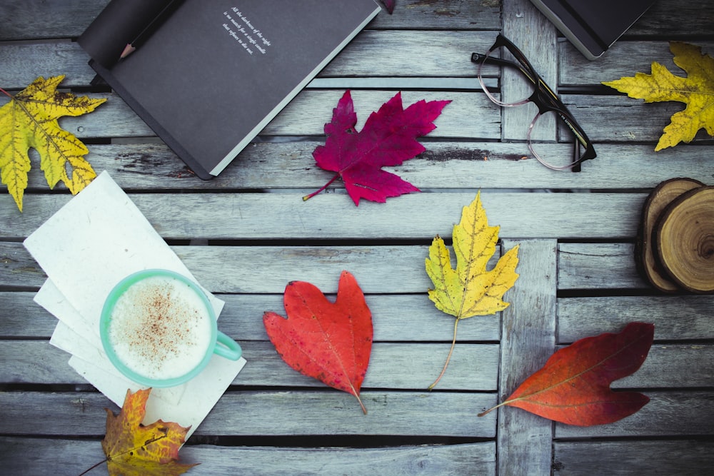 assorted-color leaves near eyeglasses, books, and green ceramic mug