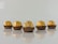 Five chocolate truffles wrapped in shiny gold foil are lined up on a reflective surface. Each piece is placed in a brown paper cup, and the lighting highlights the textures of the foil.