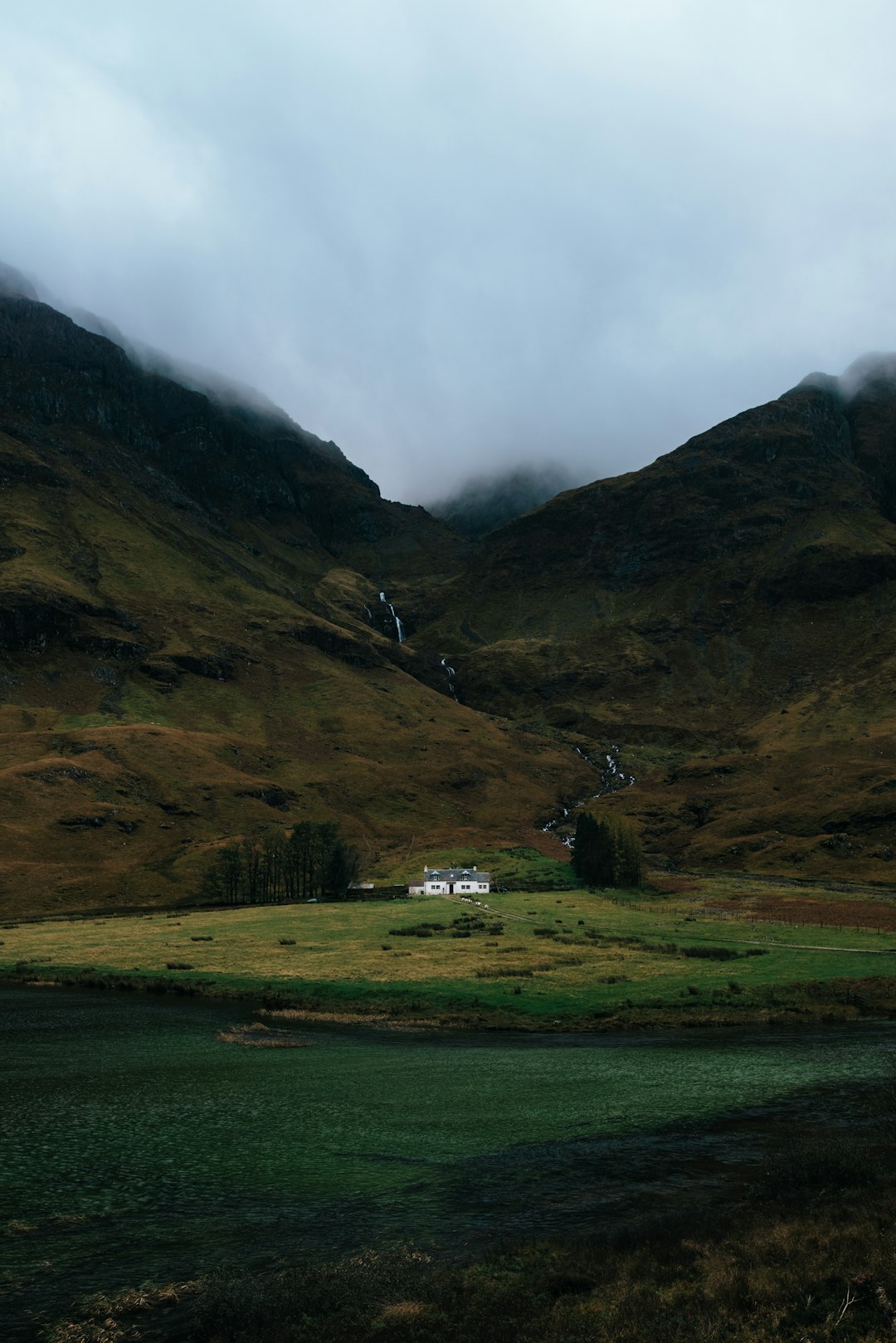 white and gray painted house below brown mountain taken at cloudy morning