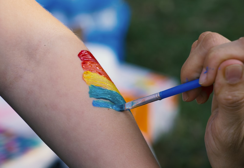 person painting rainbow on person's arm shallow focus photography