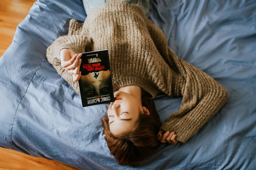 Frau im Pullover hält Buch in der Hand, während sie auf dem Bett liegt