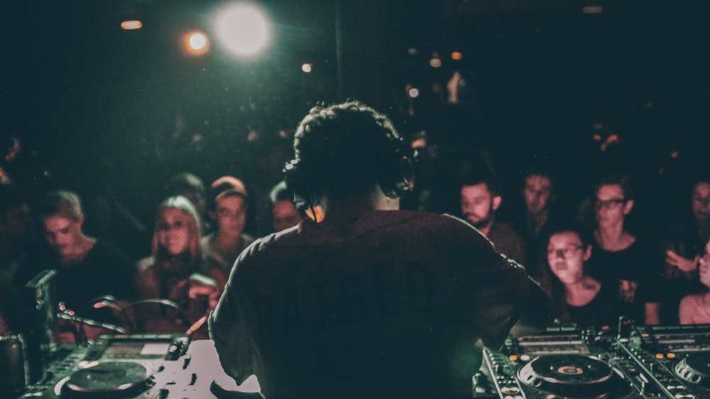 man in grey shirt operating black DJ turntable inside room