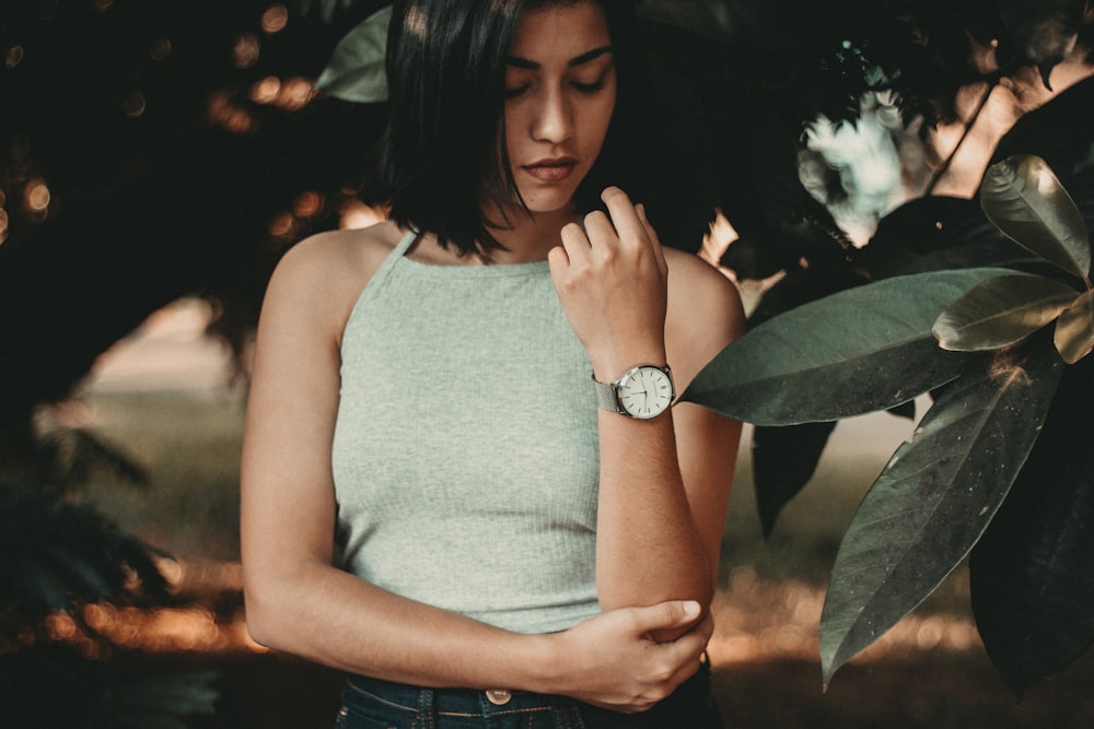 woman standing near green leaf tree while holding her elbow with her right arm