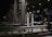 A toll booth area is depicted, featuring structures made of metal with numerous poles and booths marked with signs like S11 and S12. The setting is at night, illuminated by artificial lights, creating a stark contrast against the dark sky. The scene is largely empty with no visible vehicles or people.
