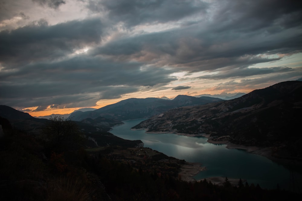 mountain beside river under gray clouds during golden hour