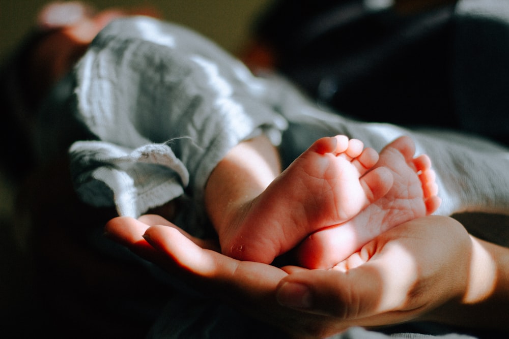 personne tenant les pieds d’un bébé