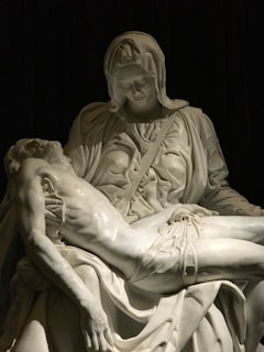 A detailed and emotionally evocative marble sculpture depicting a sorrowful figure cradling another lifeless figure, both draped in intricately carved cloth.