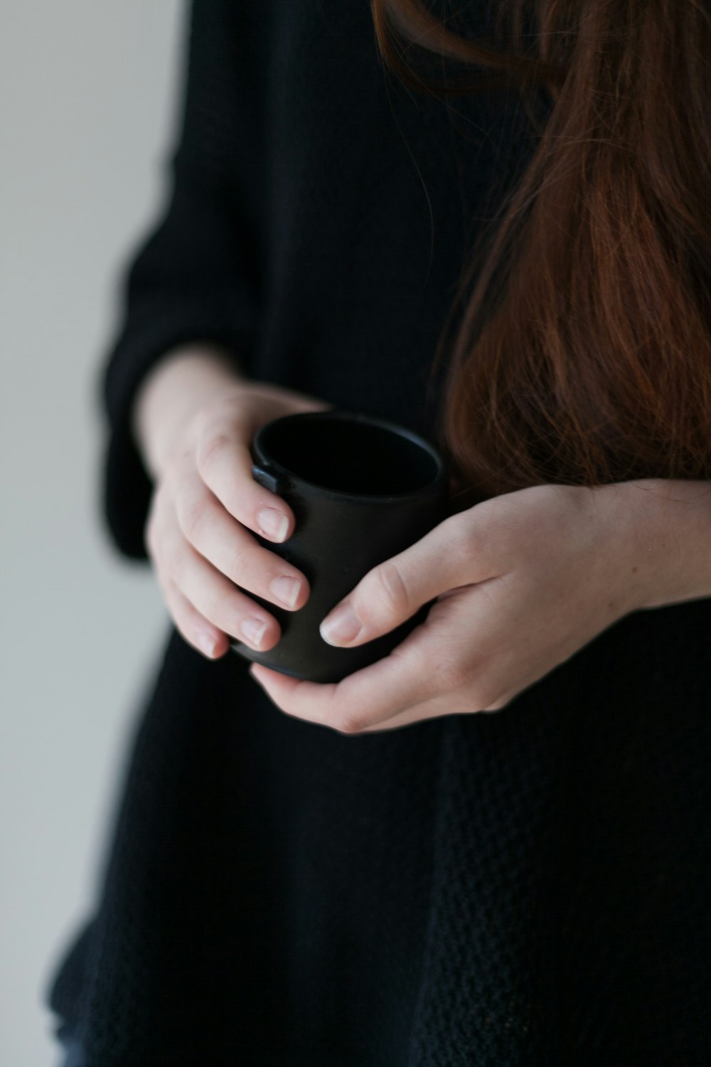 mulher na camisa preta da manga comprida segurando a caneca de cerâmica preta