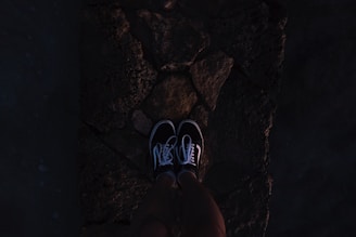 Close-up of a pair of black, customized sneakers with intricate dark-themed designs, resting on a moody concrete surface.