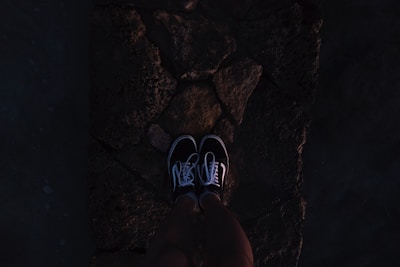 Close-up of a pair of black, customized sneakers with intricate dark-themed designs, resting on a moody concrete surface.