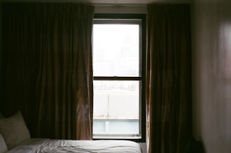 A cozy bedroom window dressed with dark gray blackout curtains softly filtering morning light.