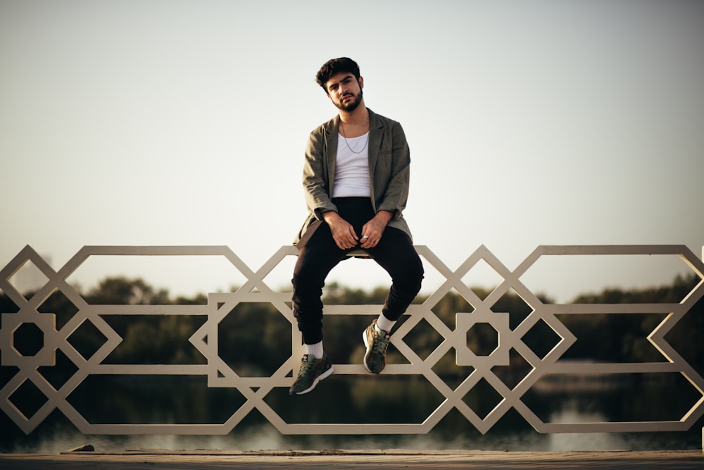 man sitting on white metal fence during daytime