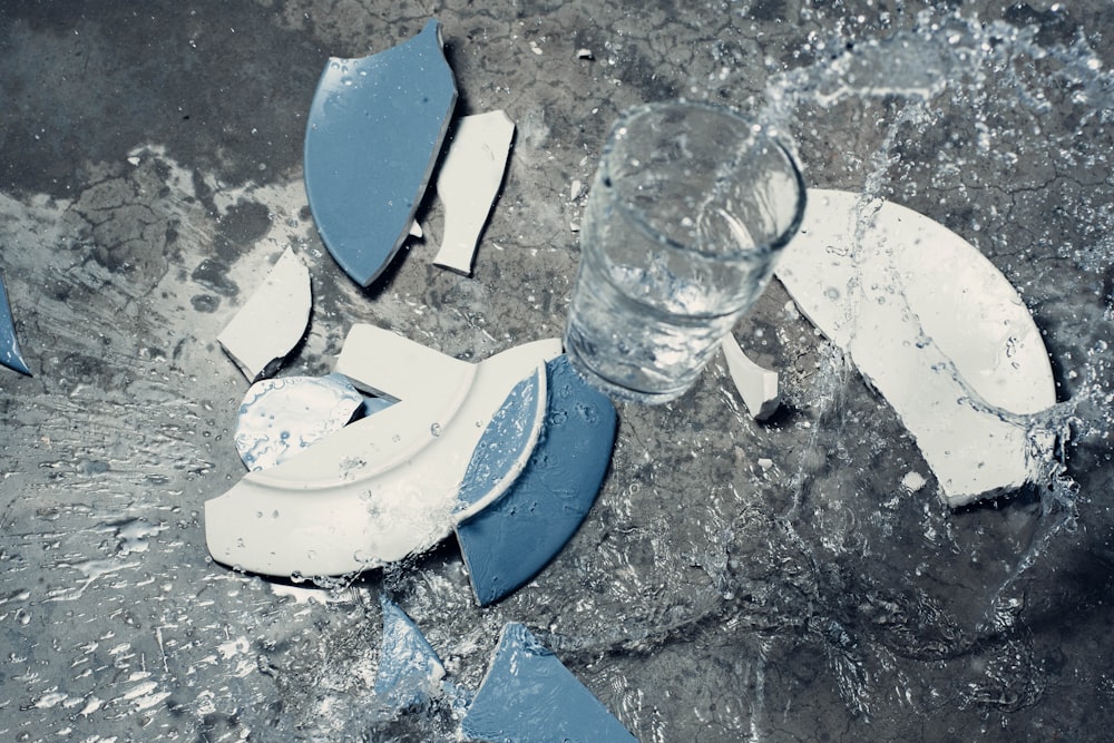 zerbrochene weiße und blaue Keramikplatte und klares Getränkeglas mit Wasser