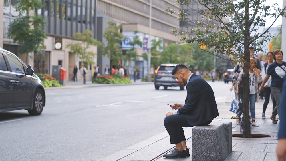 man with suit jacket sitting next to street with passing cars