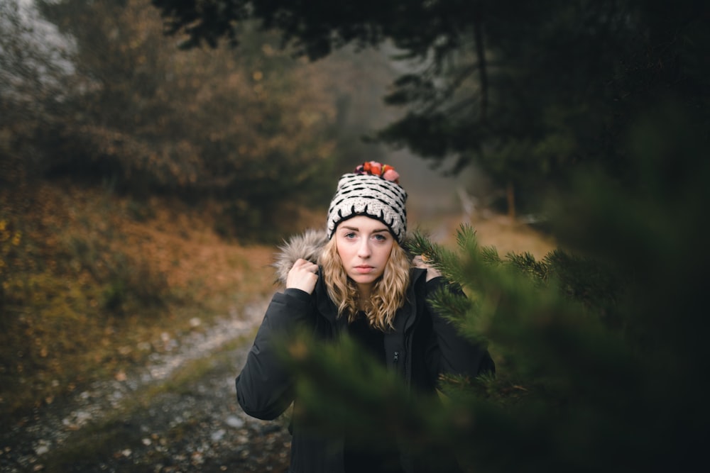 woman wearing black coat walking under trees